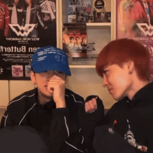 Two People Are Sitting In Front Of A Wall With A Poster That Says Thomas Now GIF