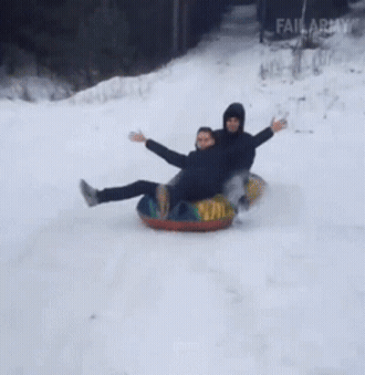 Two People Are Sledding Down A Snowy Hill On Tubes GIF