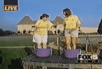 Two People Are Standing In Buckets In Front Of A Live Sign That Says Fox 5 GIF