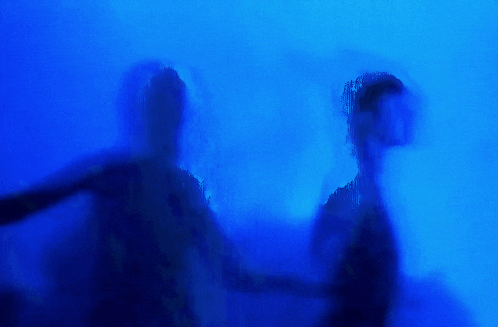 Two People Are Standing In Front Of A Lightning Bolt In A Dark Room . GIF