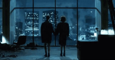 Two People At Window Overlooking City At Night GIF