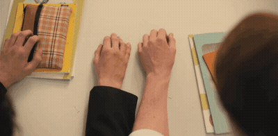 Two People Holding Hands On A Table With Books GIF