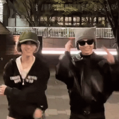 Two People In Hats And Sunglasses Dancing In Front Of Building With Fence GIF