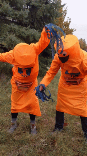 Two People In Orange Costumes With The Letter T On Their Heads GIF