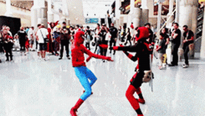 Two People In Spiderman And Deadpool Costumes Are Dancing In Front Of A Crowd GIF