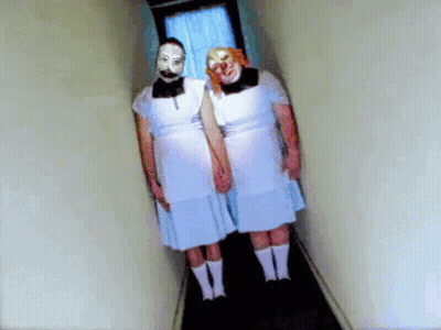 Two People in White Dresses and Clown Masks Holding Hands in Hallway