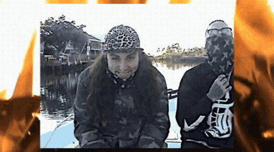 Two People On A Boat With One Wearing A Leopard Print Hat And The Other Wearing A Black Shirt With The Letter T On It GIF