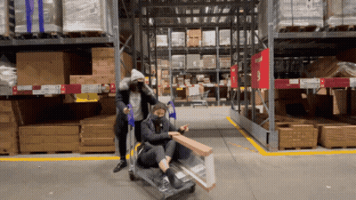 Two People Pushing Cart In Warehouse With Gtu Sign GIF