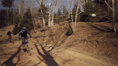 Two People Riding Bikes Down A Dirt Road GIF