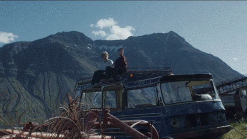 Two People Sit On The Roof Of A Blue Van GIF