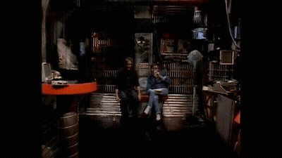 Two People Sitting On A Bench In A Dark Room With A Sign That Says ' Closed ' On It GIF