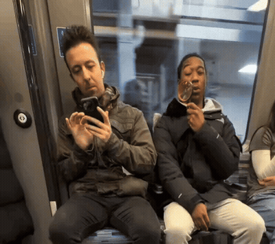 Two People Sitting On A Train With One Holding A Glass GIF