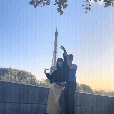 Two People Standing In Front Of The Eiffel Tower With Their Arms In The Air GIF