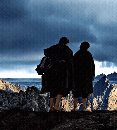 Two People Standing On Top Of A Rocky Cliff Looking Out Over A Body Of Water GIF