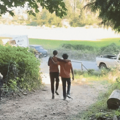 Two People Walking Down A Dirt Path With A White Truck Parked Behind Them That Says ' A ' On It GIF