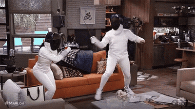 Two People Wearing Fencing Masks Are Standing In A Living Room . GIF
