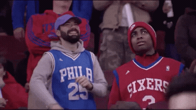 Two Philadelphia Sixers Fans Are Sitting In The Stands At A Basketball Game . GIF
