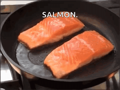 Two Pieces Of Salmon Are Being Cooked In A Frying Pan With The Word Salmon Above Them GIF
