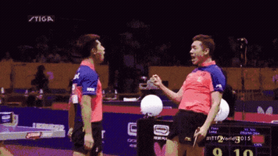 Two Ping Pong Players Are Standing Next To Each Other In Front Of A Scoreboard That Says Stiga GIF