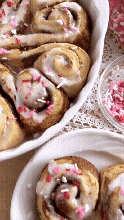 Two Plates Of Cinnamon Rolls With Icing And Sprinkles GIF