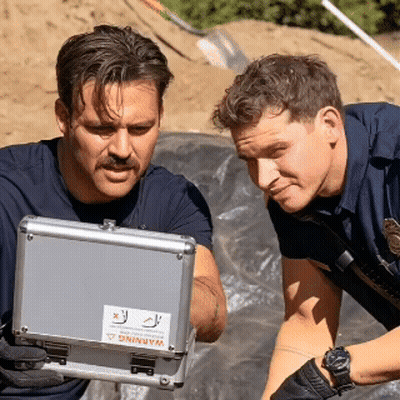 Two Police Officers Are Looking At A Case With A Warning Sticker On It GIF