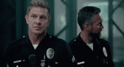 Two Police Officers Are Standing Next To Each Other In A Dark Room Looking At The Camera . GIF