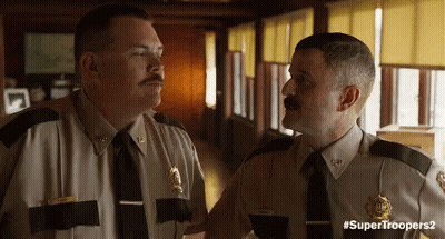 Two Police Officers Are Standing Next To Each Other In A Hallway Talking To Each Other . GIF
