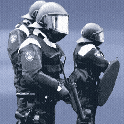 Two Police Officers Are Standing Next To Each Other With One Holding A Shield And The Other Holding A Gun GIF