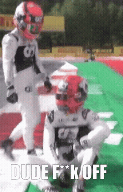 Two Race Car Drivers Are Standing On A Race Track And One Of Them Is Sitting On The Ground . GIF