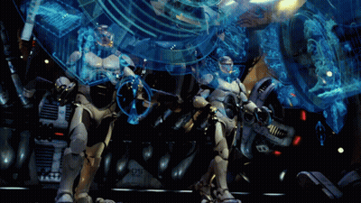Two Robots Are Standing In Front Of A Machine With The Number 05 On It GIF