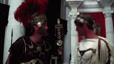 Two Roman Soldiers Standing Next To Each Other With A Sign That Says ' S.r.o.m. ' On It GIF