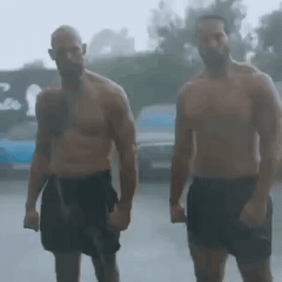 Two Shirtless Men Are Standing In The Rain Holding Hands . GIF