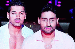 Two Shirtless Men Are Standing Next To Each Other In A Dark Room GIF