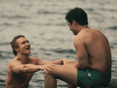 Two Shirtless Men Sitting In Water Talking GIF