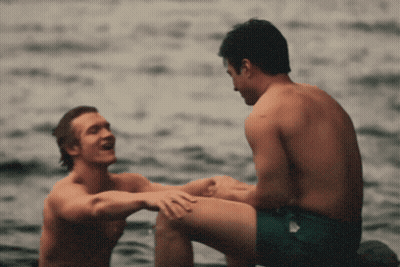 Two Shirtless Men Sitting In Water Talking GIF