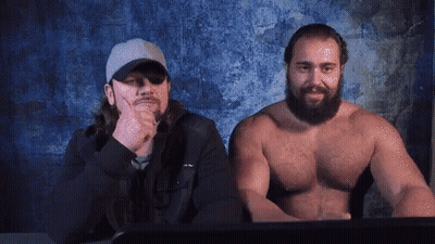 Two Shirtless Men Sitting Next to Computer Screen