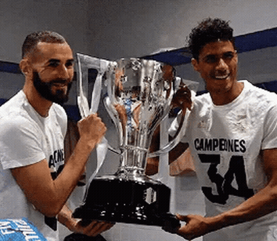 Two Soccer Players Are Holding A Trophy In Their Hands . GIF