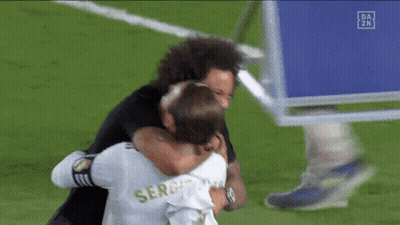 Two Soccer Players Are Hugging Each Other On A Field . GIF
