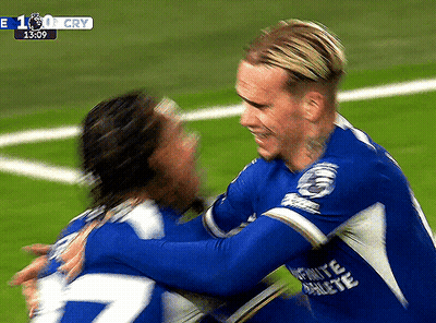 Two Soccer Players Are Hugging Each Other On A Field With A Score Of 1:0 GIF