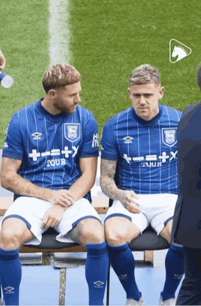 Two Soccer Players Are Sitting On A Bench And One Has A Shirt That Says Tour GIF