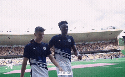 Two Soccer Players Are Walking On A Field With A Sign That Says Heitse On It GIF