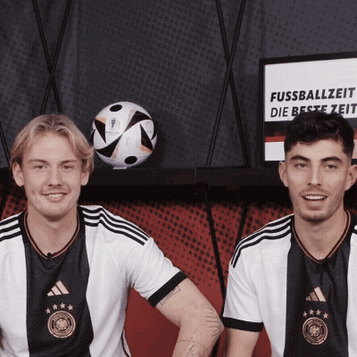 Two Soccer Players Next To Fussballzeit Sign GIF