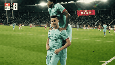 Two Soccer Players On A Field With A Scoreboard In The Background That Says 1318 GIF