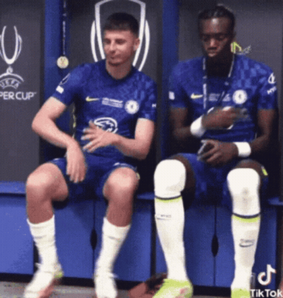 Two Soccer Players Sitting On Bench In Locker Room GIF