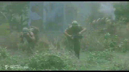 Two Soldiers Are Walking Through A Field Carrying A Rifle . GIF
