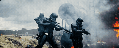 Two Soldiers Holding Guns In Front Of Burning Building With Letter M On Helmets GIF
