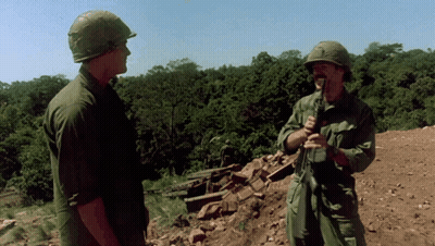 Two Soldiers In Front Of A Thatched Hut With Explosion GIF