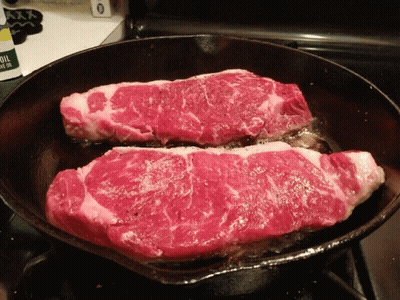 Two Steaks Are Being Cooked In A Cast Iron Skillet GIF
