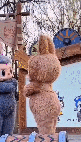 Two Stuffed Animals Are Standing Next To Each Other In Front Of A Sign . GIF