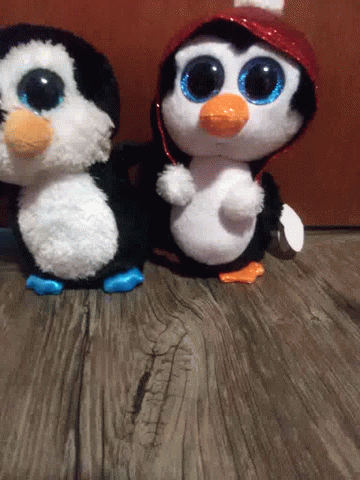 Two Stuffed Penguins Are Standing Next To Each Other On A Wooden Table . GIF